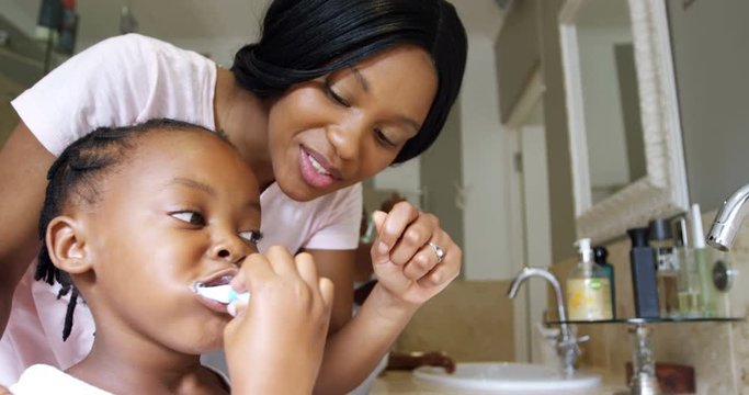 Mother teaching her daughter to brush her teeth in bathroom 