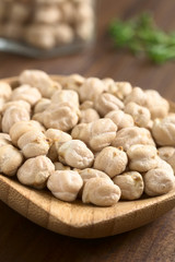 Raw chickpeas or garbanzo beans on small wooden plate, photographed with natural light (Selective Focus, Focus one third into the image)