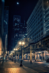 Fototapeta na wymiar City street at night in Chicago's Loop with elevated train station, illuminated buildings, cars and moon..