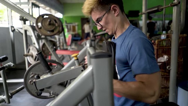 Closeup of a teen bodybuilder straining to pull large weights on a universal gym.