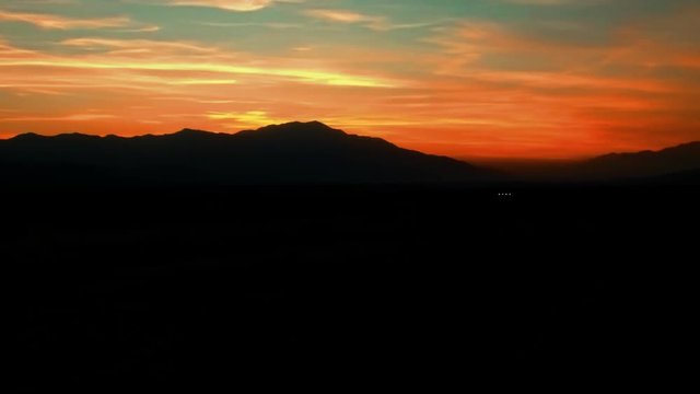 Panning aerial shot of mountains silhouetted against a sunset zooming out