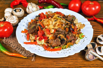 Pasta with roasted meat and vegetables on wooden table