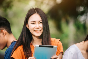 Fototapeta premium A young or teen asian girl student in university smiling and reading the book and look at the tablet or labtop computer in summer holiday.