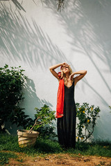 the girl in the red shawl and black dress standing next to a white wall, the shadows from the palm trees