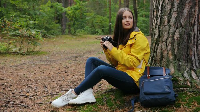 Young amazing woman sitting at the tree and taking photos of the nature on the vintage camera in the green forest. Outdoors