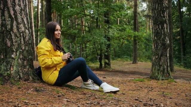 Sporty woman hukung alone in the forest, sitting on the ground and taking photos of the nature on the vintage camera. Outdoors.