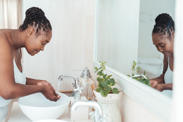 Young African woman washing her face in the bathroom sink