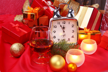 Christmas clock, glass with cognac or whisky and candles. New Year's Decoration with gift boxes, christmas balls and tree. Celebration Concept for New Year.