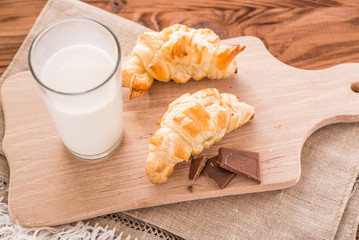 freshly baked croissants on a wooden cutting board with a glass of milk. Tasty breakfast