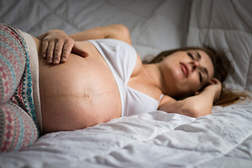 Obraz na płótnie Canvas A pregnant young girl is sleeping and holding her hand on her stomach. Focus on the abdomen