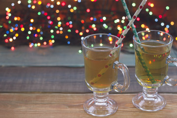 Festive still life with two glass cups of green tea with patterned straws on a colored wooden table against dark bokeh background