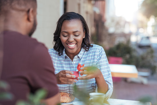 Smiling young African woman opening a gift from her boyfriend