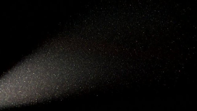 Particle of dust flies on a dark background in the light of a bright spotlight