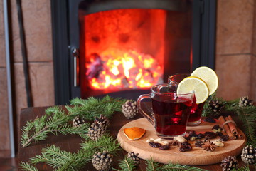 Mulled wine. A couple of mugs of mulled wine on a wooden table among the fir branches in front of the fireplace.