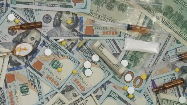 Pills, drugs, cocaine, syringe on dollar bank notes. Paper money rotation.