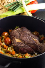 Suppenfleisch in einem Suppentopf mit Suppengemüse im Hintergrund