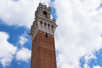Obraz premium Detail of the Torre del Mangia 87 m. (Tower of Mangia) on blue sky with clouds. Siena, Italy