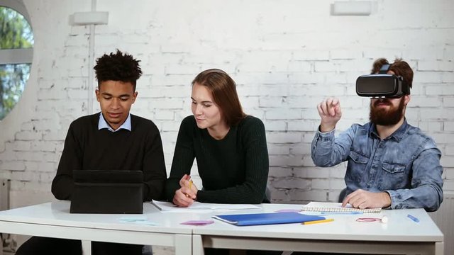 Multiethnic group of people working together. One of them is using vr glasses. Happy diverse group of students or young business team working on a project. Slowmotion shot