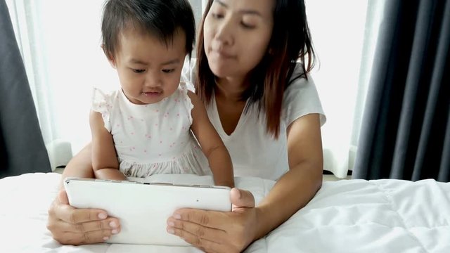 4k of Mother and baby playing with digital tablet in the bedroom