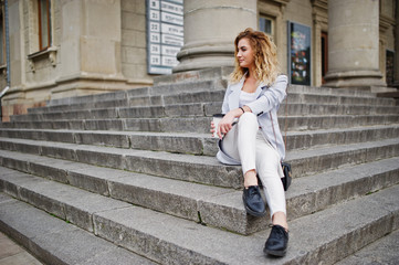 Fototapeta na wymiar Stylish curly blonde model girl wear on white with cup of coffee posing on stairs outdoor.