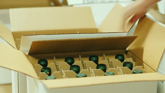 Workers put bottles of wine in cardboard boxes. Packaging of finished products, preparation for shipment
