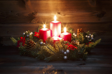 Fourth Advent - Decorated Advent wreath with four red burning candles on a wooden background with festive atmosphere