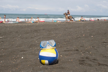 Ball and swimming glasses on beach. Blurred photo of people on sand beach. Travel or sea vacations concept