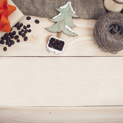 Light wooden christmas background with coffee beans, toy christmas tree and a gift box with a bow, square