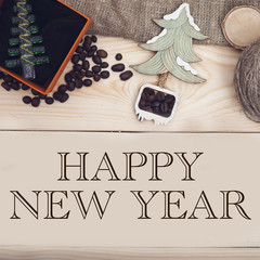 Happy New Year inscription, coffee beans, a toy Christmas tree in an orange box with a black velvet bottom, a wooden Christmas tree on a light wooden background, top view