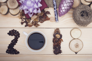 2018 inscription of coffee beans, cup, dry flowers and wooden slices, a dark purple gift box with a violet bow, a purple pinecone and a skein of threads, light wooden background, top view