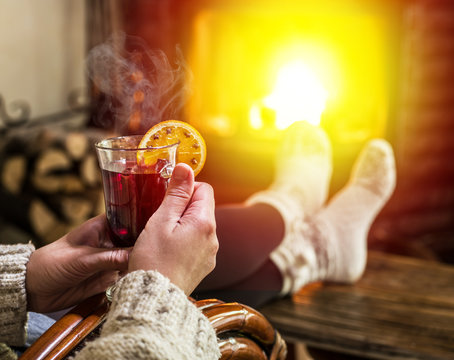 Hot mulled wine and book in woman hands. Relaxing in front of burning fire in the cold winter day.