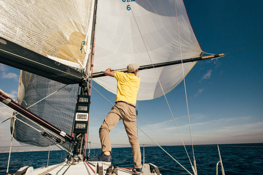 Professional sailor or yachtsman uses mast and forestay to put up spinnaker or mainsail on racing competition yacht or sailboat on warm summer day