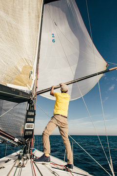 Professional sailor or yachtsman uses mast and forestay to put up spinnaker or mainsail on racing competition yacht or sailboat on warm summer day