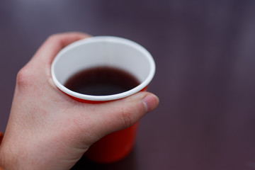 Picture of man's hand holding red paper glass with tea