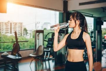 Fototapeta na wymiar Asian woman exercising in the gym, Young woman workout in fitness for her healthy and office girl lifestyle. She is drinking fresh water.
