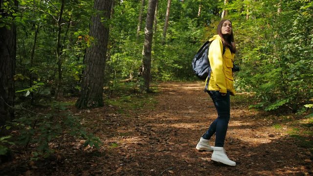 Back view of the young sporty woman tourist with the vintage camera roaming alone in the beautiful green forest and turning around to the camera. Outdoors