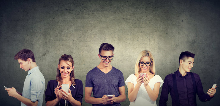 young people in casual clothes using mobile phone standing together against concrete wall 