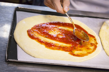 Cooking pizza, adding crushed tomatoes on pizza dough. Closeup.