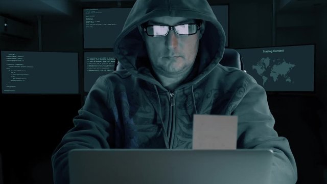 White caucasian man in hood and fashion glasses coding program for internet. Man tale stiker from monitir screen of laptop. Many monitors at backgrouns in room