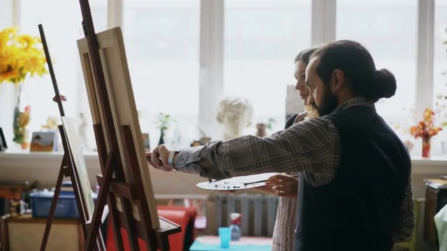 Skilled artist man teaching young girl to drawing paintings and explaining the basics in art studio