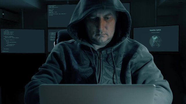 White caucasian man in hood and fashion glasses coding program for internet. Write task make memo. Man stick stiker to monitir screen of laptop. Many monitors at backgrouns in room