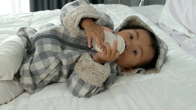 4k of Cute baby drinking milk a bottle in white bed