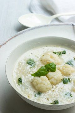 Vegane Blumenkohlsuppe mit Kokosmilch mit frischem Basilikum in einer weißen Suppenschale mit Suppenlöffel