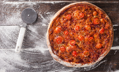 Rustic homemade pizza with сherry tomatoes. Top view on wooden table with flour
