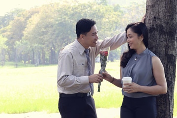 Businesswoman eating coffee and relax in the garden before going to work. Boyfriend show love with red roses. Both of them plan to marry. Use as background and texture. Valentine's Day