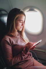 Girl is reading from smartphone in airplane near window