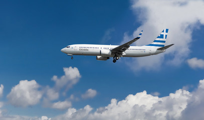 Commercial airplane with flag of Greece on the tail and fuselage landing or taking off from the airport with blue cloudy sky in the background
