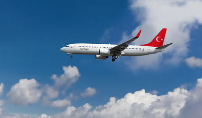 Fototapeta na wymiar Commercial airplane with Turkish flag on the tail and fuselage landing or taking off from the airport with blue cloudy sky in the background
