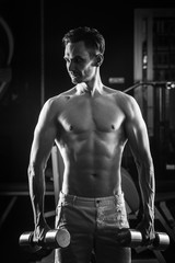 Fototapeta na wymiar Strong Muscular man with naked torso abs working out in gym with dumbells. Black and white photo.