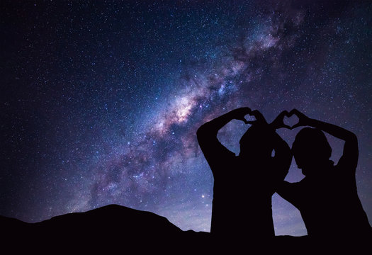 People makes heart symbol by hand with Milky Way and night sky on background.